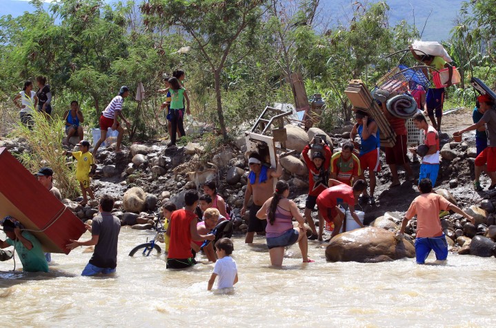 Colombianos deportados da Venezuela carregam seus pertences às margens do rio Táchira