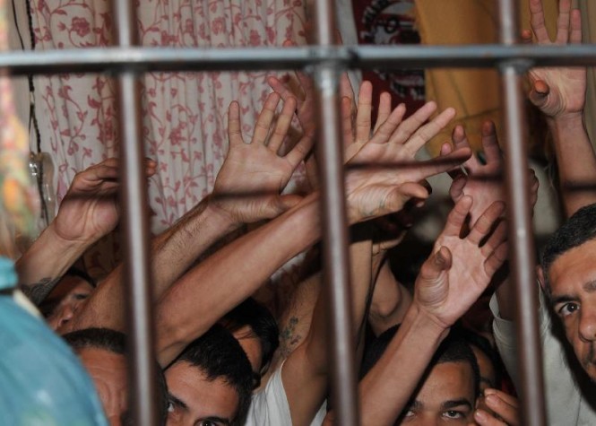 Prisioneiros levantam os braços na cela