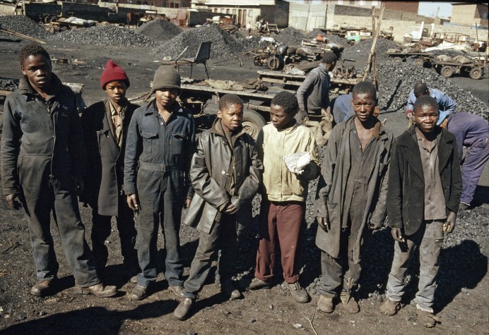 Crianças sul-africanas, com roupas velhas e sujas, estão enfileiradas no meio de uma mina de extração de carvão 
